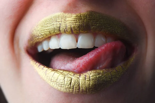 Sexy tongue licking lips. Sensual happy smiling woman mouth. Golden lipstick. Glamour luxury gold mouth. Gold paint on lips. Golden lips on woman mouth. Metallic body. Gold concept