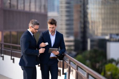 Finansal büyüme, çevrimiçi iş. Takım elbiseli iki iş adamı dışarıda kredi kartı ve laptop tableti tutuyor. Hesabı öde. Şehirde kredi kartı olan bir adam. İş anlaşması. E-para. Başarı işi