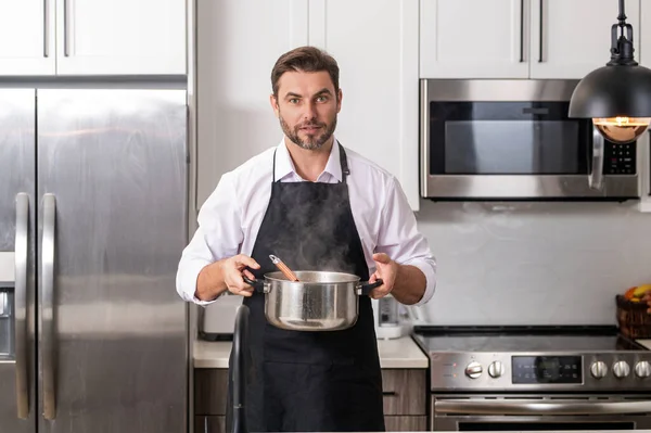 Man cook cooking at kitchen. Chef cook prepares a dish with food in saucepan. Menu recipe healthy food. Man cooking at home preparing food in kitchen. Mature man standing in kitchen, preparing food