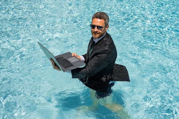 Funny business man relaxing in suit on swimming pool. Summer vacation, business on sea beach. Summer rest, business people concept. Wealthy business man relaxing in swimming pool. Remote on-line work