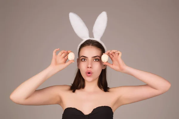 Beautiful young woman with bunny ears and Easter eggs on studio background. Festive bunny and easter eggs season. Stylish woman in Easter bunny ears isolated on studio background