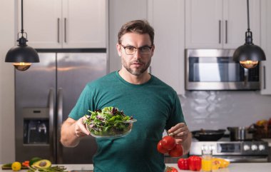 Mutfakta bir tabak sebze salatası olan bir adam. Adam mutfakta vegan sağlıklı salata pişiriyor. Modern mutfakta sebzeli milenyum adamı, akşam yemeği ya da öğle yemeği için taze sebze salatası hazırla.