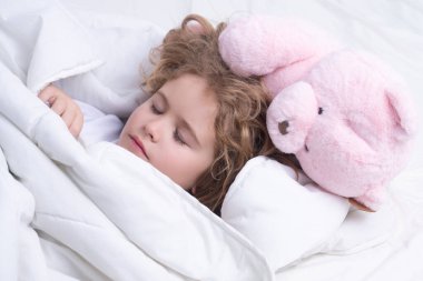 Çocuk tatlı rüyalar görüyor. Çocuk oyuncak ayıyla uyur, uyur. Çocuk yatakta uyuyor.