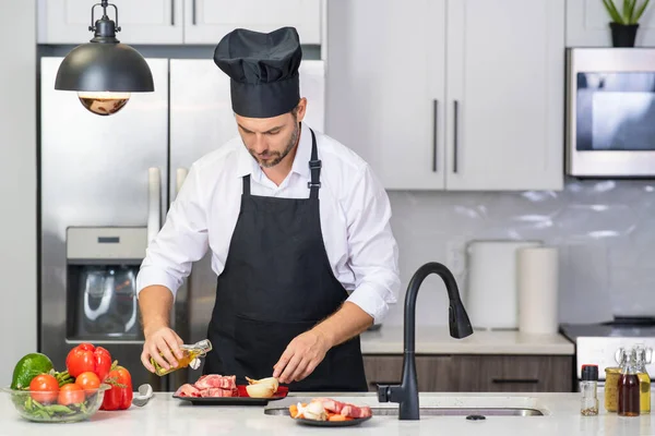 シェフ成熟した男は台所でエプロンを調理します 台所で食べ物を準備するハンサムな男 おいしい食事を作る男 肉や野菜とキッチンの男 ポートレートのカジュアル男でエプロンでキッチン — ストック写真