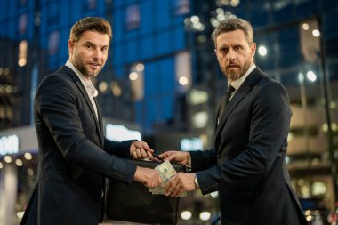Takım elbiseli yatırımcılar dolar banknotları veriyor. İş adamı dışarıdaki ortağına para veriyor. İş adamı para veriyor. İş ortaklığı. Parası olan zengin bir iş adamı. Para verme kavramı
