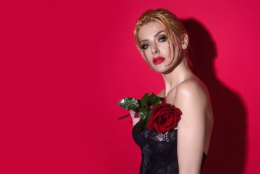 Kırmızı stüdyo arka planında izole edilmiş kırmızı güller tutan çekici, sevimli, hayalperest kızın portresi.