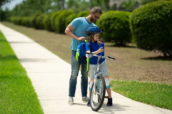 Father and son concept. Father teaching son riding bike. Father helping son to ride a bicycle in american neighborhood. Child in safety helmet learning to ride cycle with his dad. Fathers day
