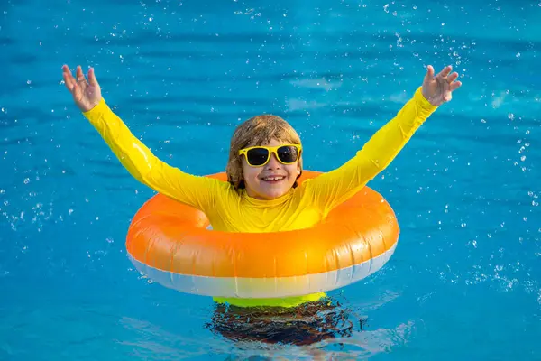 在游泳池里戴着橡皮圈的小男孩 夏天的乐趣 小孩子在游泳池里游泳 在游泳池里的孩子孩子们在充气环上放松地游泳 暑假的概念 — 图库照片