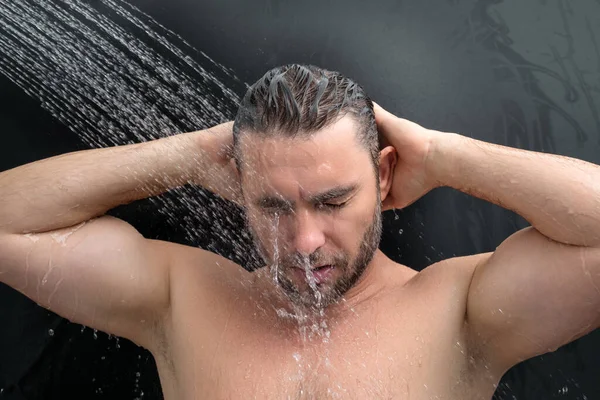 Man taking a shower. Washing hair with shampoo under water falling from shower head. Morning routine guy showering. Body care hygiene shower. Man is under water drops in shower. Wellness and spa