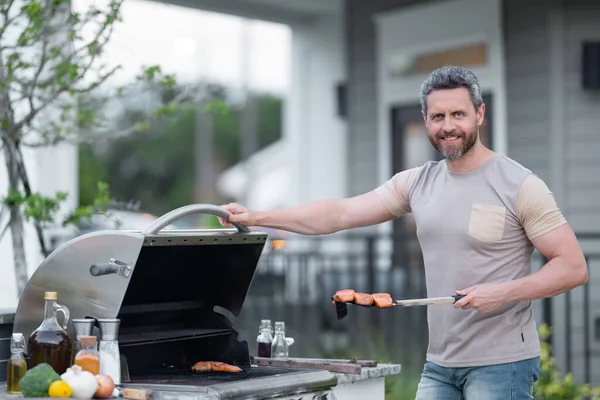 Middle aged man preparing barbecue grill outdoor. Man cooking barbecue grill at backyard. Chef preparing food on barbecue. Millennial man grilling meat on barbecue grill. Bbq party. Meal grilling