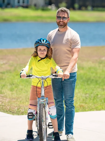 Happy Fathers day. Father and son in bike helmet for learning to ride bicycle at park. Father helping son cycling. Father and son on the bicycle on summer day. Kid son trying to ride bike with father