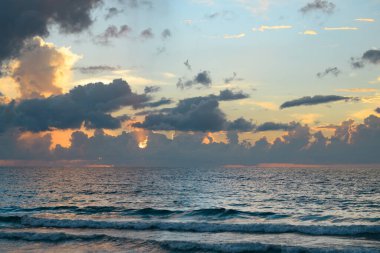 Gökyüzü ve bulutların arasından güneş batarken deniz batıyor. Okyanus ve gökyüzü arkaplanı, deniz manzarası.