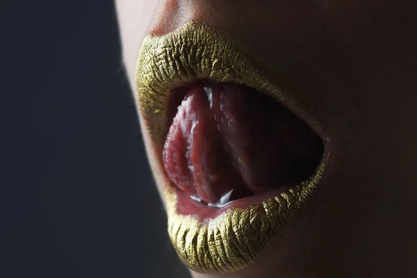 Sensual tongue licking lips. Woman mouth close up. Golden lipstick. Glamour luxury gold mouth. Gold paint on lips. Golden lips on woman mouth. Metallic body. Gold concept