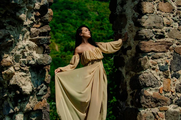Woman, fashion model on fortress, old castle stones wall. Girl in a fashion dress outdoor