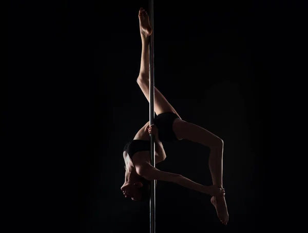 Flexible girl does gymnastic exercises on pylon for stretching. Beautiful sexy flexible woman demonstrates sexy flexible body. Flexibility stretching on black. Flexible female body. Pole dance