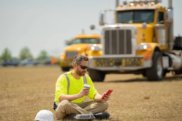 Worker taking break from work drinking coffee and resting sitting on grass. Builder worker relaxed after work on coffee break. Worker break relax time. Worker on lunch break. Truck driver