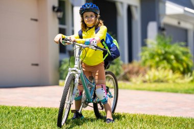 Parkta bisiklete binen sportif bir çocuk. Bisiklet süren kasklı çocuk. Çocuk bisiklet sürmeyi öğreniyor. Bisikletli çocuklar. Kasklı mutlu çocuk dışarıda bisiklet sürüyor. Çocuklarla spor eğlencesi.