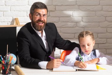 İlkokul öğrencisi ve sınıfta eğlenceli bir öğretmen. Öğrenci kız öğretmeniyle sınıfta yazıyor. Okul malzemeleriyle özel ders alan sevimli bir kız.