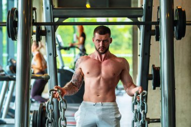 Spor salonunda kaslarını şişiren yakışıklı, kaslı, beyaz bir adam. Fitness ve vücut geliştirme sporu. Spor salonunda dambılı olan vücut geliştirici, sıkı çalışma.