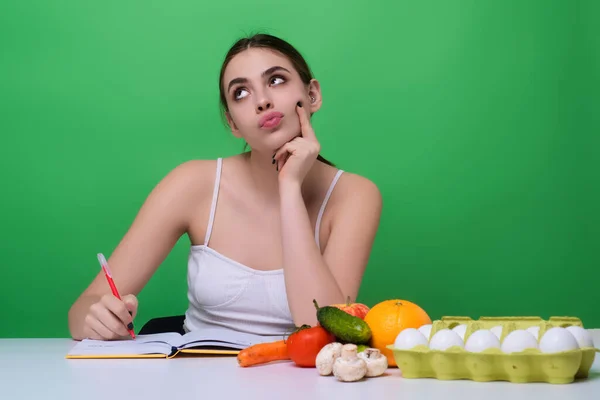 Girl writing diet plan on table and using vegetables. Girl eating vegetable diet salad in studio. Vegan salad. Female on diet. Dieting concept. Healthy lifestyle. Diet for weight loss