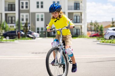 Parkta bisiklete binen sportif bir çocuk. Bisiklet süren kasklı çocuk. Çocuk bisiklet sürmeyi öğreniyor. Bisikletli çocuklar. Kasklı mutlu çocuk dışarıda bisiklet sürüyor. Çocuklarla spor eğlencesi.