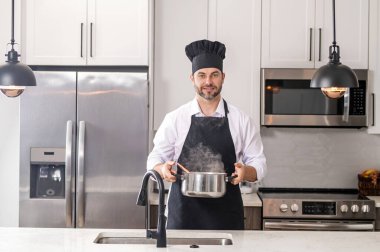 Erkek aşçı ya da aşçı mutfakta tencerede yemek pişiriyor. Gurme yemeği hazırlama süreci. Adam evde yemek pişiriyor, esrar kullanıyor. Şef yemek pişiriyor. Yakışıklı aşçı aşçı konsepti