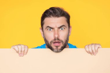 Stüdyo arka planında boş tahtası olan kızgın bir adam yüzü. Öfkeli adam boş tabelayı kopyalayarak gösteriyor. Fikir ve teklif. Reklamınız. Metin ve maket için boş alanı olan boş reklam panosu