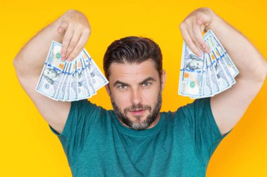 İzole edilmiş sarı arka planda dolar banknotlar halinde nakit para tutan adam. Bir sürü banknotla birlikte iş adamının stüdyo portresi. Dolar parası konsepti. Kariyer zenginliği işi. Nakit Dolar