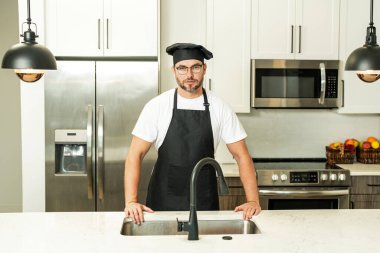 Mutfakta şef üniforması giyen yakışıklı orta yaşlı bir adam. Aşçılık ve aşçılık. Restoran menüsü konsepti. Yemek servisi, yemek pişirme, yemek reklamcılığı. Üniformalı adam mutfakta.