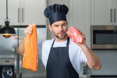 Chef with raw meat beef and fish salmon fillet on kitchen. Chef man in uniform on kitchen. Handsome man chef in uniform with chef hat cooking raw meat beef and fish salmon fillet in the kitchen