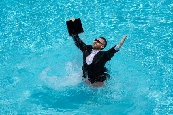 Freelance work, distance online work, e-working. Summer business. Business man in suit excited jumping with laptop in pool. Business man work online. Humor business concept