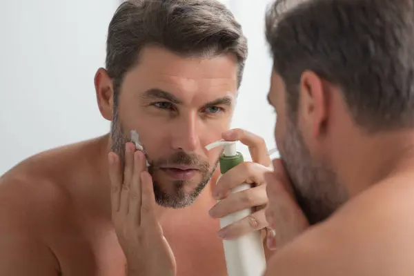 Skin care. Beauty middle aged man applying face cream. Male spa hold face cream. Facial cream, moisturizing lifting nourishing creme. Face cream for skincare. Wrinkle cosmetic facial treatment