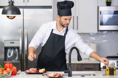 Modern mutfakta yemek pişiren çekici bir adam. Evde yemek pişiren yakışıklı adam mutfakta salata hazırlıyor. Modern mutfakta yemek hazırlayan sıradan bir adam. Olgun bir adam mutfak masasında yemek hazırlıyor.