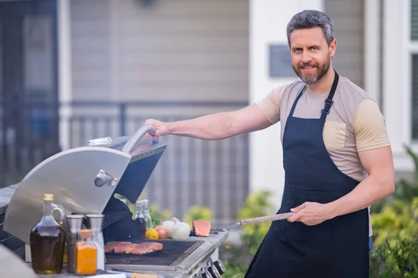 バーベキューの準備をしてる40代の男 男性はバーベキューグリルで肉を調理します 男はバーベキューで肉を調理夏の家族の夕食のために家の裏庭で — ストック写真
