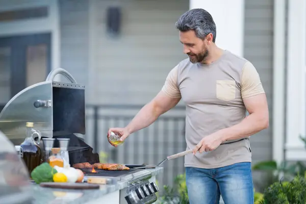 烧烤的概念 中年男人穿着T恤衫烧烤 烤和烤食物 户外烤肉 烤肉和烤肉后院里煮肉 — 图库照片