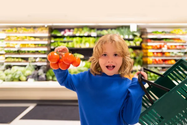 Child with fresh tomato vegetables. Kid is choosing fresh vegetables and fruits in the store. Child buying food in grocery supermarket. Buying in grocery store. Groceries in the supermarket