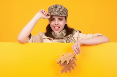 Güz sonbaharı modasına uygun giyinmiş hippi bir genç kadın şık bir şapka ve eşarp takıyor. Güzel kız sonbahar yapraklarını yüzüne yakın tutar, stüdyo arka planında izole olur. Akçaağaç yaprağıyla sonbahar kadınının portresi