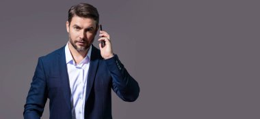Gri stüdyoda izole edilmiş cep telefonu kullanan takım elbiseli bir iş adamı. Cep telefonu kullanan orta yaşlı bir iş adamı portresi. Akıllı telefonu olan bir iş adamı, iş görüşmesi. Pankart
