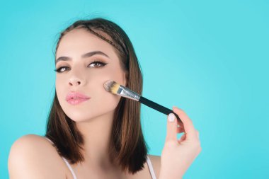 Beautiful young woman applying makeup on studio background. Pretty girl holding makeup brushes and make up on face with cosmetics. Facial beauty. Perfect skin, natural make up clipart