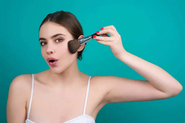 Woman hold blush blusher apply powder visage isolated over studio background. Girl powdering cheeks. Makeup brush. Female model gets blush powder on the cheekbones