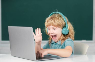 Kulaklıklı komik çocuk internetten ders çalışıyor, kulaklıklı çocuk internetten ders alıyor. Heyecanlı çocuk duyguları.