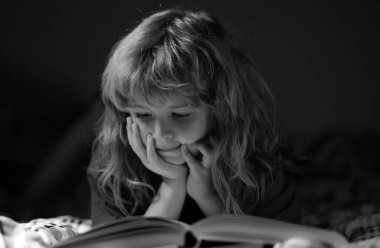 Yatakta uzanmış kitap okuyan sevimli bir çocuk. Çocuk yatmadan önce kitap okuyor. Hayal gücü ya da öğrenme kavramı