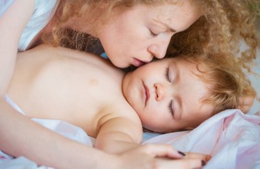 Anne ve bebek yatakta uyuyor. Anne uykulu çocuğu öpüyor. Çocukluk ve aile kavramı, kapalı mekan portresi.