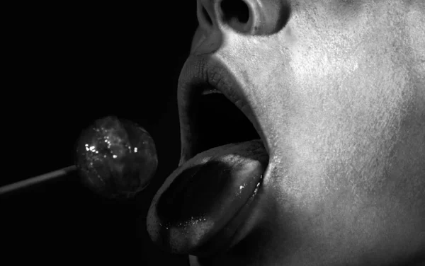 Lollipop in the mouth, close-up. Beautiful girl mouth with lolli pop. Glossy red woman lips with tongue. Mouth lick suck chupa chups on neon lights