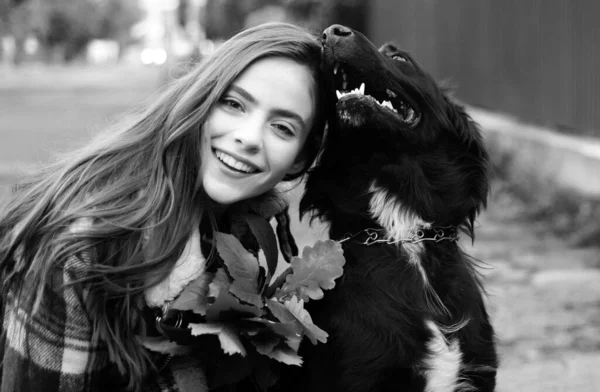 Pretty young girl with big black dog smiling outdoors. Real emotion cheerful portrait cuddling dog pet human. Autumn mood