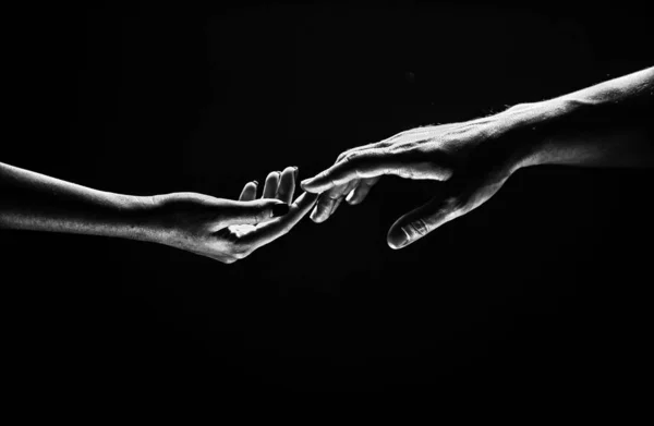 Romantic touch with fingers, love. Two hands stretch each other, black background. Couple in love holding hads, close up. Helping hand, support, friendship. Tenderness, tendet touch