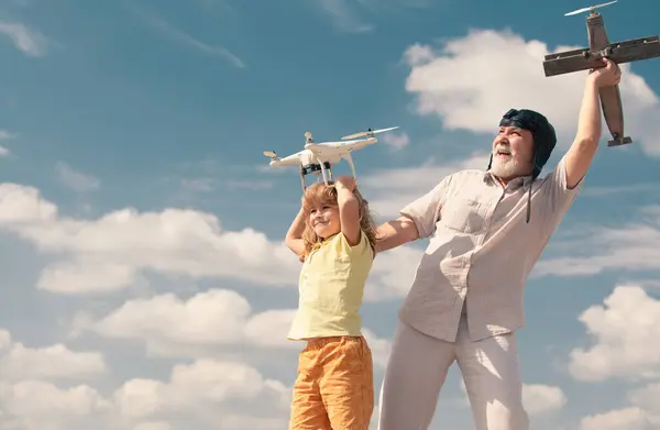 Grandfather and son hold plane and drone quad copter against sky. Child pilot aviator with plane dreams of flying