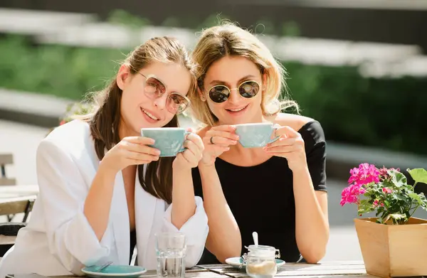 Romantic woman friends with coffee cup in cafe. Spending good time with best friend. Two beautiful women in sunglasses drinking coffee outdoors in vintage cafe. Attractive french women