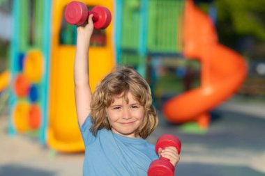 Yaz sporu, çocuklar oyun alanında spor eğitimi. Kol kaslarını halterle şişiren sevimli çocuk. Dambılı spor çocukları.