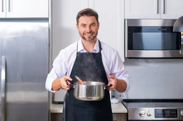 Man cook cooking at kitchen. Chef cook man prepares a dish with food in saucepan. Menu recipe healthy food. Man cook food in modern kitchen. Mature man standing in kitchen, preparing food
